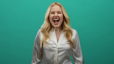 Sarışın genç bir kadın neşeli bir şekilde yeşil bir arka plana gülüyor. Bulaşıcı bir gülümsemesi var. Rahat bir atmosferde..