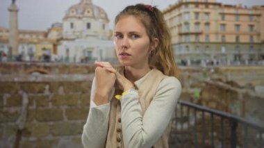 Elleri kenetlenmiş bir kadın şehir manzarasında endişeli görünüyor genç sarışın figürü şehir harabelerini keşfederken şehir mimarisini gezerken..