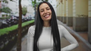 Güneşli bir günde şehir mimarisi tarafından çevrelenmiş bir caddede İspanyol kadın açık havada gülümsüyor..