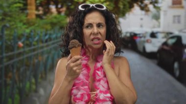 Orta yaşlı kadın dondurma külahını tutuyor ve sokakta diş ağrısı için yanağa dokunuyor; diş ağrısı rahatsızlığı.