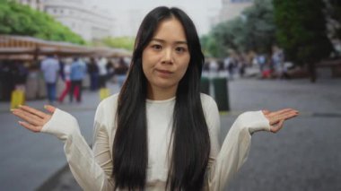 Kalabalık bir şehir pazarında, açık havada dikilen, günlük beyaz giysiler giyen, canlı bir caddede insanlar ve dükkanlar tarafından çevrili bir kadın..