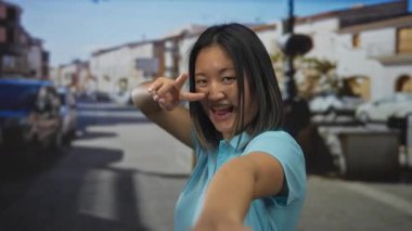 Çinli bir kadın şehir caddesinde neşeli bir zafer jesti yapıyor. Canlı bir ifadeyle ve şehir geçmişiyle kamerayı işaret ediyor..