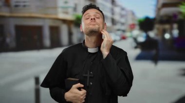 Arka planda bulanık binalar ve geleneksel siyah bornoz ve çapraz kolye giyen şehir sokaklarında İncil 'i elinde tutan bir rahip..