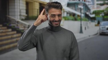 Gri balıkçı yaka kazaklı modern sakallı adam şehir caddesinde parmak ucuyla geziyor..