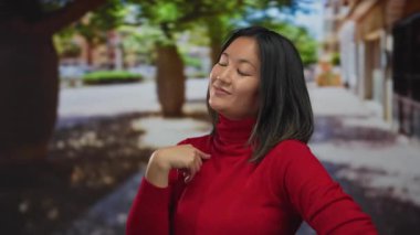 Canlı bir şehir caddesinde kırmızı süveter giymiş bir kadın, canlı, güneşli bir ortamda şehir dışından kendine güvenen bir tutum sergiliyor..