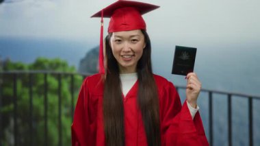 Avustralya pasaportlu kırmızı mezuniyet elbisesi giyen kadın deniz kenarına karşı küresel fırsatları sembolize ediyor ve sahilde akademik başarıyı kutluyor..