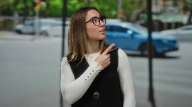 Gündüz vakti hareket halindeki arabalar ve yeşil ağaçlarla çevrili kalabalık bir caddede dururken iki elini gösteren bir kadın..