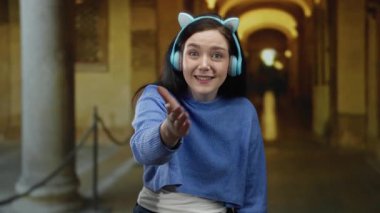 Üniversite kampüsü koridorunda gülümseyen ve elini uzatan kulaklık takan bir kadın..