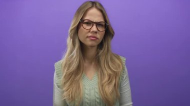 Gözlüklü ve yeşil kazaklı sarışın kadın mor stüdyo takımında kaşlarını çatıyor. Hayal kırıklığı şüphesi..