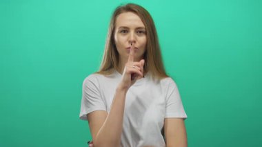 Yeşil arka planda sessizce susan bir kadın, düşünceli bir ifadeyle günlük beyaz bir gömlek içinde sessizliğini koruyor.