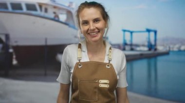 Limanda kahverengi önlüklü bir kadın, arkasında büyük bir tekne ve açık hava altında okyanus manzarasıyla açık deniz atmosferini yakalıyor..