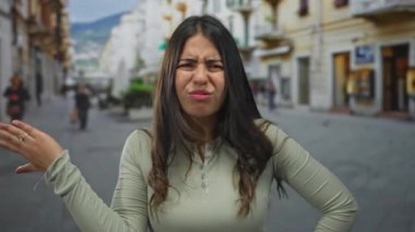 Kalabalık bir sokakta şaşkın bir ifadeye sahip genç bir kadın, açık gökyüzü altındaki insanlar ve binalarla çevrili bir şehir ortamında kargaşayı işaret ediyor..