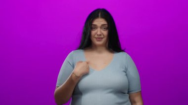 Genç bir kadın, kendine canlı pembe arka planda işaret ederken, kendine güveni olan bir gülümsemeyle anlaşmazlığını dile getirirken el kol hareketi yapar..