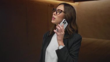 Akıllı telefondan konuşan İspanyol kadın gözlüklü ve spor ceketli modern odada teknoloji ile duygusal ve nişanlı..