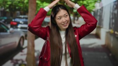 Şehir sokağında kırmızı ceketli bir kadın açık havada eğlenceli jestler yapıyor çağdaş moda özgüvenini gösteriyor