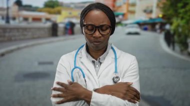 Beyaz önlüklü ve gözlüklü doktor bir şehir caddesinde, soğuk görünüyor, kolları çapraz ve boynunda bir steteskop var..