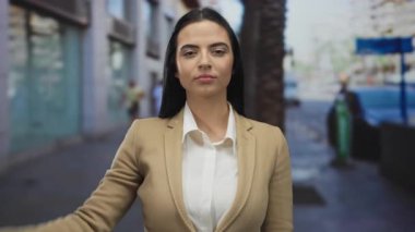 Yoğun bir caddede selamlama yapan genç bir kadın, resmi bir takım elbise giyip, dinamik bir şehir ortamının özünü yakalarken profesyonellik ve güven yayıyor..
