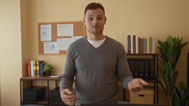 Ofiste gülümseyen bir adam kitaplarla ve bitkilerle rafların yanında duran süveter giymiş modern kendine güvenen ifadeyle sohbet ediyor..