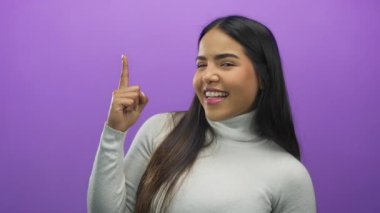 İzole edilmiş stüdyo ortamında parlak bir şekilde gülümseyen parlak bir süveter giyen canlı mor arka planda parmakları olan bir kadın.