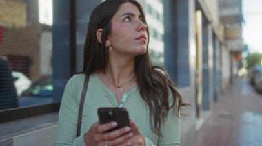 Şehirdeki sokak ortamında akıllı telefon kullanan bir kadın şehir yaşamının ortasında cep telefonuyla meşgul olan düşünceli, genç bir İspanyol kadını sergiliyor..