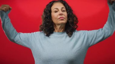 Kıvırcık saçlı, kırmızı arka planda kollarını esneten güçlü olgun bir kadın özgüven ve güçlenmeyi vurguluyor..