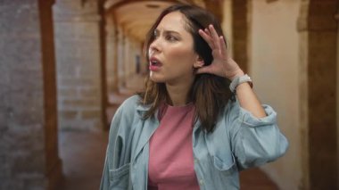 Üniversite koridorundaki kadın dikkatle dinliyor, merak ve mimari ortama olan ilgisini çekiyor..