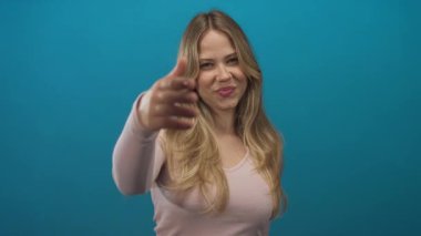 Sarışın beyaz kadın stüdyoda elini ileri uzatıyor; arkadaşlığı karşılama daveti.