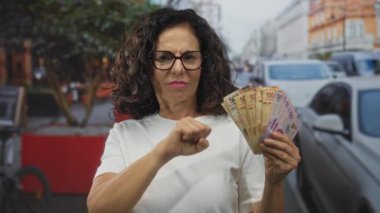 Orta yaşlı İspanyol kadın Meksika pesoları ve banknotları elinde tutan kalabalık sokaktaki kameraya yumruğunu uzattı..