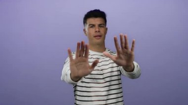 Genç adam mor bir arkaplan karşısında el kol hareketi yapıyor. Alkışlamaktan yüzünü kaplamaya kadar farklı ifadeler sergiliyor. Çizgili bir gömlek giyiyor, çeşitli duygular gösteriyor..