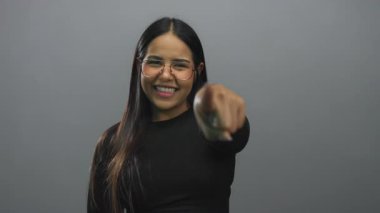 Gri arka planda neşeli bir tebessümle canlı ve anlamlı bir poz yakalayan bir kadın..