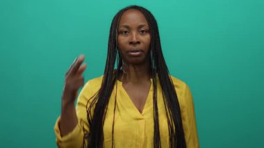 Sarı gömlekli, uzun örgülü bir kadın yeşil bir arka plana karşı düşünceli bir şekilde el kol hareketi yapar. Alnında parmak ve yakın planda ifadesel bir yüzle duyguları tasvir eder..