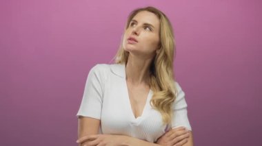 Düşünen ve poz veren pembe bir arka plan, uzun sarı saçlar ve günlük beyaz kıyafetler, duygu ve bireysellik taşıyan bir kadın..