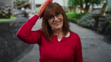 Kırmızı kazaklı son sınıf öğrencisi kadın elinde buz torbasıyla şehir sokaklarında gülümsüyor.