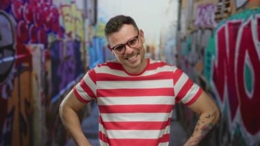 Şehir ortamında grafitiyle gülümseyen, çizgili gömlek ve gözlük takan bir adam..