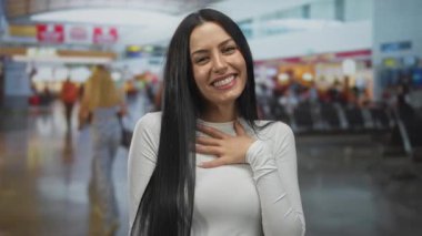 Havaalanında gülümseyen bir kadın, hareketli bir arka planı olan, yoğun terminal ve oturma alanlarında seyahat etmeye hazır ve mutlu bir şekilde..