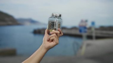 Deniz kenarında Amerikan doları ve sikkeleriyle el ele tutuşup güneşli bir kumsal sahnesini yakalıyoruz..