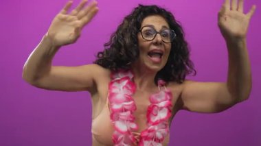 Orta yaşlı, bikinili, İspanyol bir kadın ve Hawaii Lei 'si stüdyoda çıplak kollarını sallıyor..