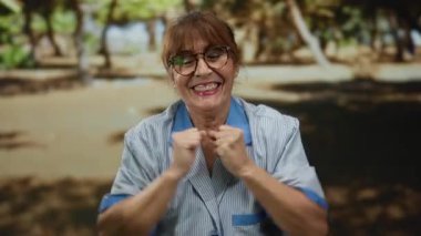 Arka planda ağaçlarla dolu bir parkta gülümseyen kıdemli İspanyol kadın..