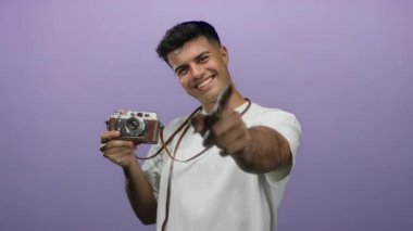 Elinde klasik kamera olan gülümseyen adam, gençlik coşkusu ve yaratıcılığını sergileyen mor arka plan karşısında izleyiciyi işaret ediyor.