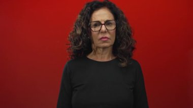 Orta yaşlı İspanyol kadın bir stüdyoda kırmızı duvara karşı çıplak yumruklarını kaldırıyor..