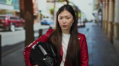 Kırmızı ceketli kadın şehir sokaklarında duruyor. Geçmişi bulanık. Şehirde hareket ve enerji hissi var..