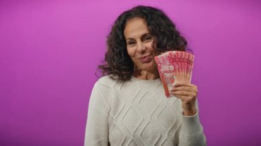 Mor bir duvara gülümseyen Çin Yuanı banknotları tutan kadın, mutluluğun ve finansal başarının bir ifadesini sergiliyor..