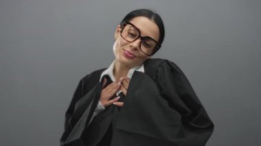 Siyah cüppeli ve gözlüklü İspanyol kadın yargıç, adaletin ve merhametin altını çizerek, gri bir zemine karşı sıcak bir jest sunuyor..