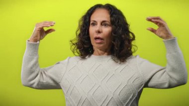 El hareketleriyle konuşan, kazak giyen, kıvırcık saçlı, olgun bir güzelliği olan, hayat dolu sarı arka planda yalnız bir kadın.