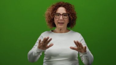 Katı yeşil duvar arka planına sakince el hareketleriyle iletişim ve sükunetini ifade eden ve rahat bir ortamda gözlük takan bir kadın..