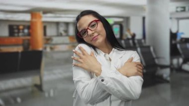 Üniformalı İspanyol kadın bilim adamı, kapalı bir havaalanı ortamında gülümseyerek seyahat koşuşturmasının ortasında sıcaklığı ve pozitifliği simgeliyor..