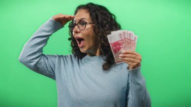 Icelandic Krona banknotları tutan orta yaşlı bir kadın canlı yeşil bir duvara bakıyor, merak ve heyecan taşıyor..