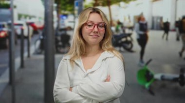 Şehir trafiğinin ortasında sarı saçlı, kırmızı gözlüklü ve hareketli şehir sokağında kendine güvenen bir kadın ve açık havada canlı bir ortam öneren bulanık yayalar.