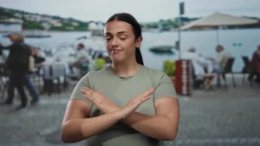 Açık hava restoranında terasa çıkmayan, manzaralı arka planı olan, sıradan kıyafetler giyen, suyun kenarında kahve içen insanlar arasında durmaktan hoşlanmadığının sinyalini veren bir kadın..