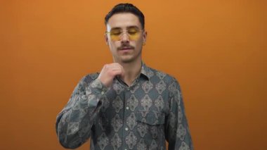 İspanyol gömlekli ve gözlüklü bir adam gerçekçi turuncu duvarlara karşı nazikçe yumruğunu dinlendirirken modern ve içsel bir manzara yaratıyor..